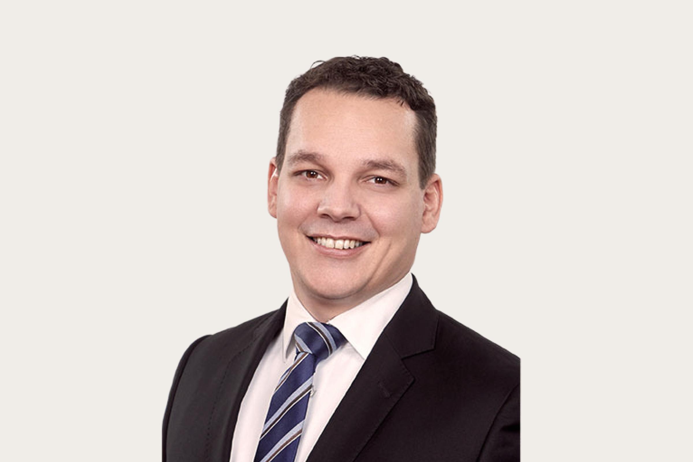 Björn Pfortner, Chief Operating Officer bei Enzo, trägt einen schwarzen Anzug und lächelt in die Kamara