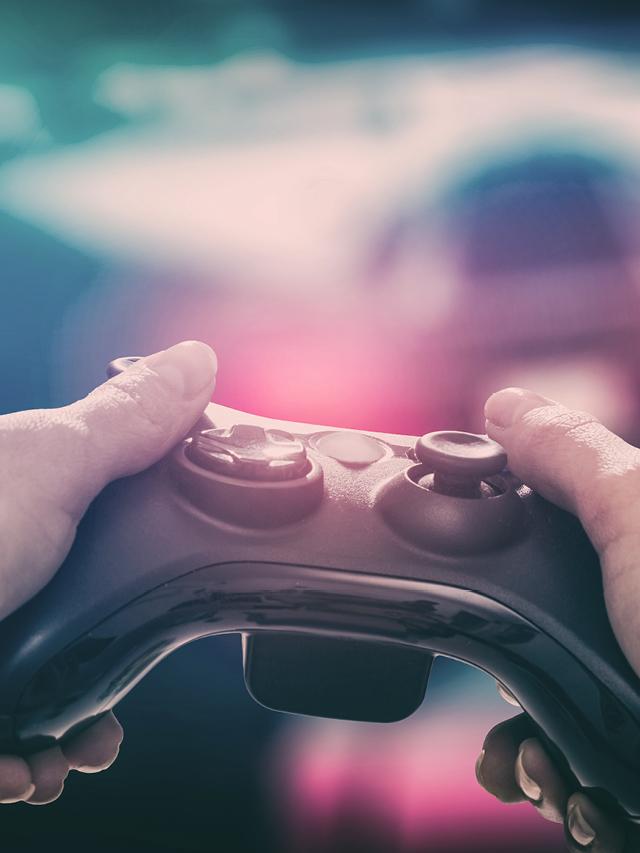 Eine Person hält einen Videospiel-Controller mit beiden Händen, während im Hintergrund ein Rennspiel auf einem Bildschirm zu sehen ist.