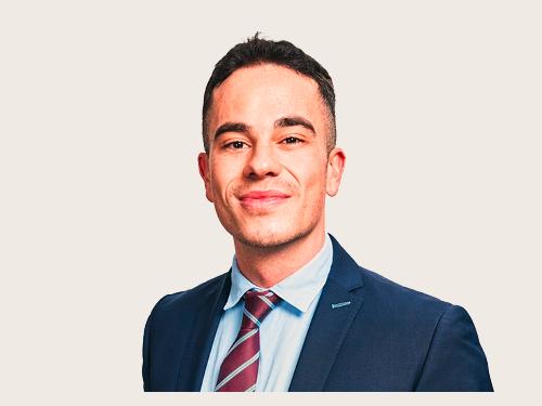 Tim Morgenstern von Control Risks. Mann mit kurzem dunklen Haar und Anzug, der lächelnd in die Kamera blickt.