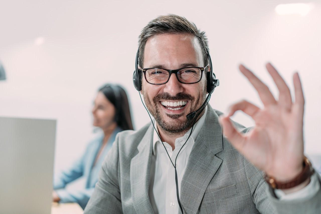 Vertriebsmitarbeiter mit Headset lächelt in die Kamera und zeigt einen Daumen nach oben.