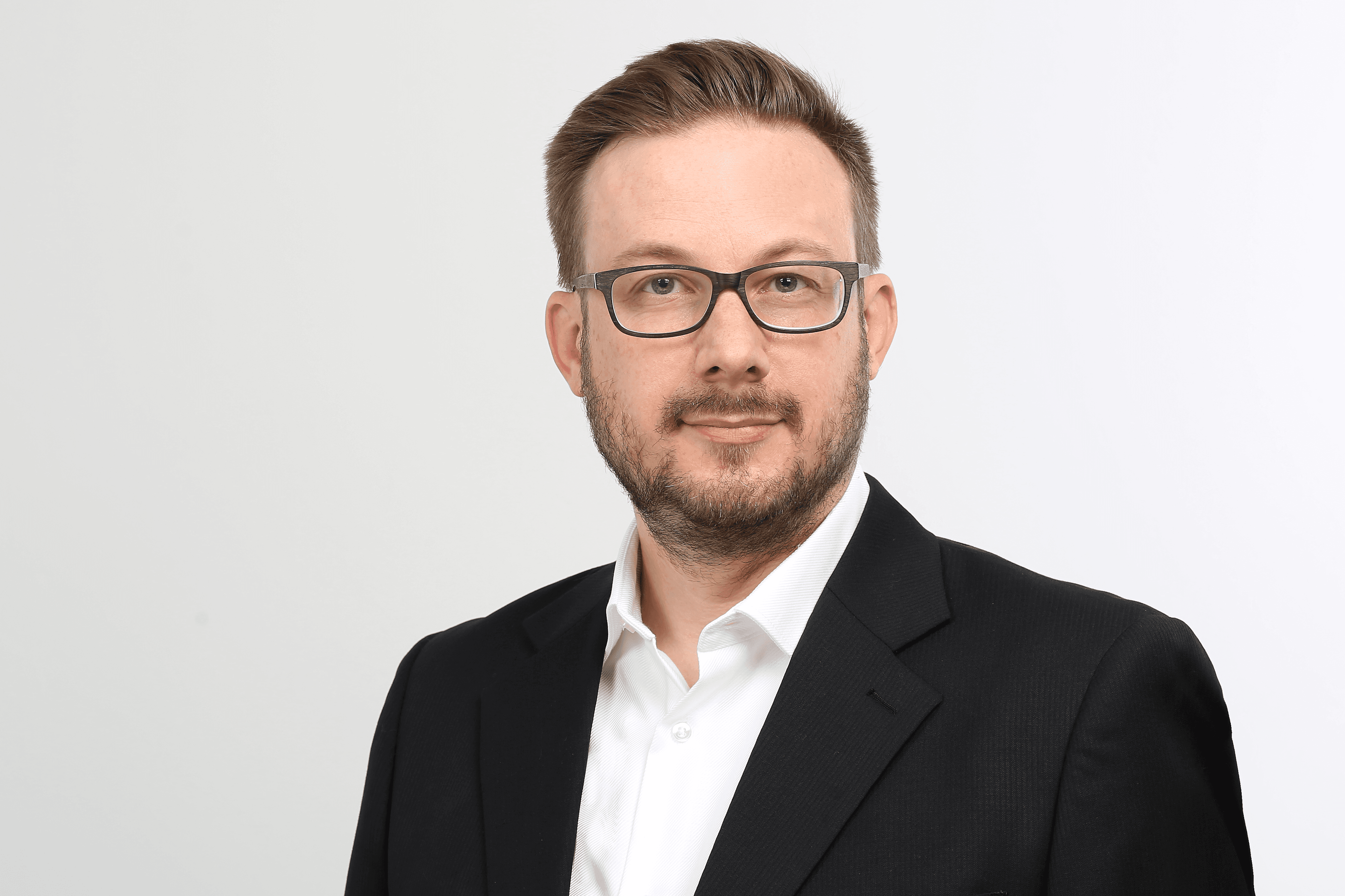 Leo Molatore, ein Mann in einem schwarzen Anzug und weißem Hemd, steht vor einem weißen Hintergrund.