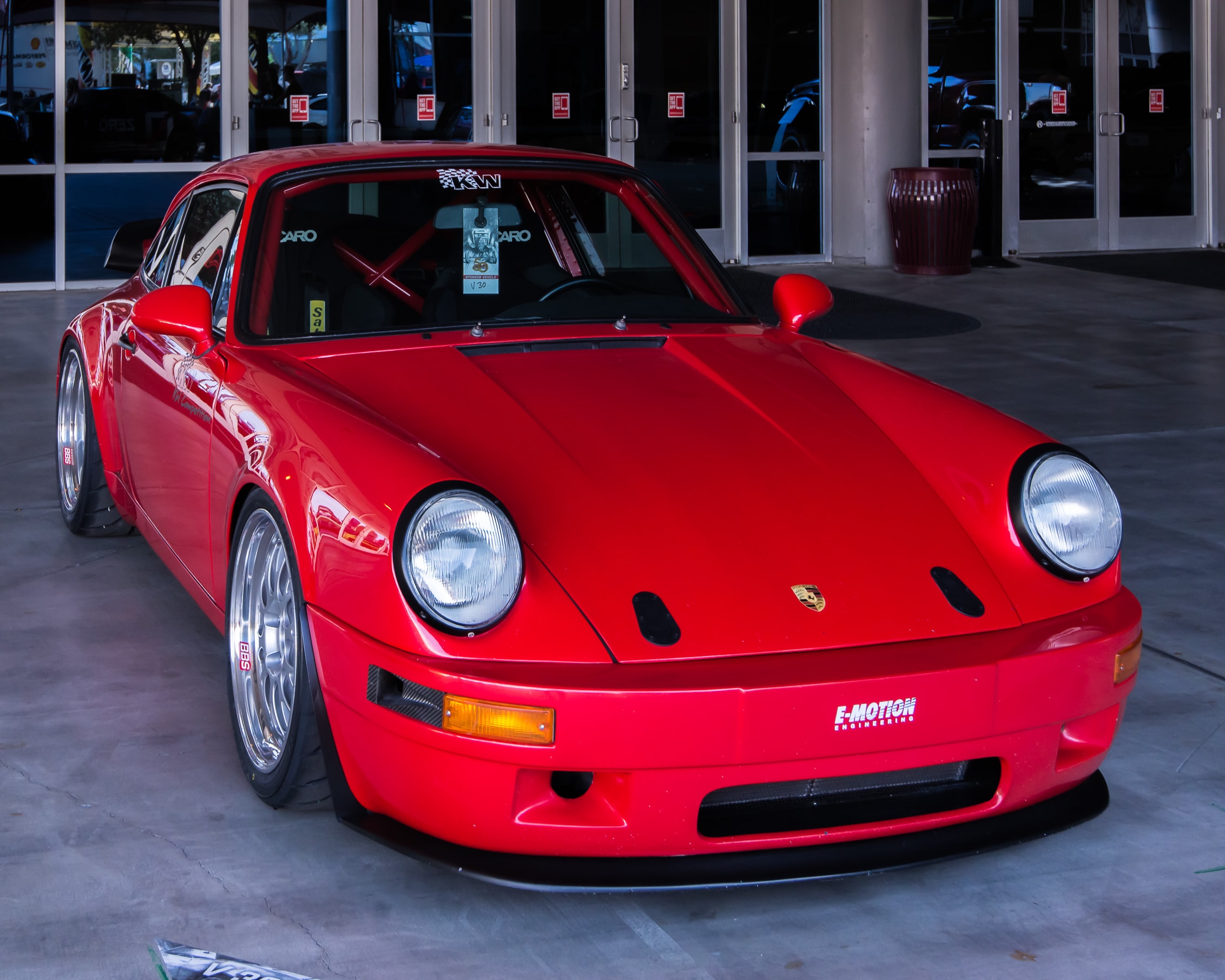 Parkender roter Porsche Carrera 911 Turbo steht vor einem Office-Gebäude. Der Oldtimer parkt schräg seitlich, sodass Seite und Front sichtbar sind.