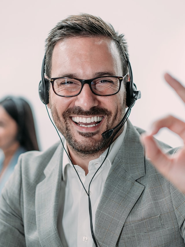 Vertriebsmitarbeiter mit Headset lächelt in die Kamera und zeigt einen Daumen nach oben.