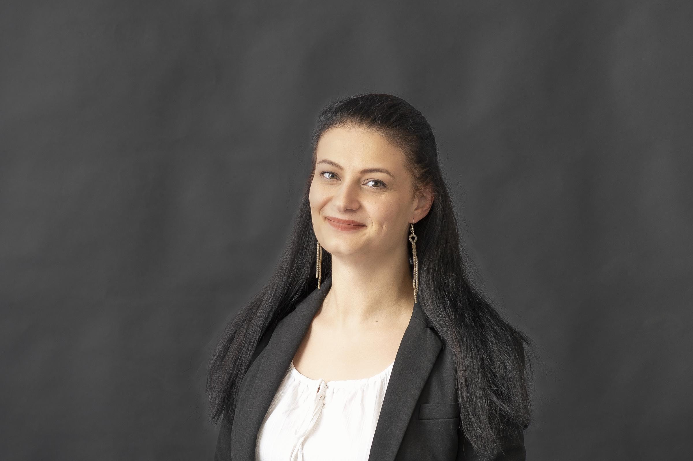 Selina Ziegler Carl Rieck, eine Frau mit langen schwarzen Haaren, trägt einen schwarzen Blazer über einem weißen Oberteil.