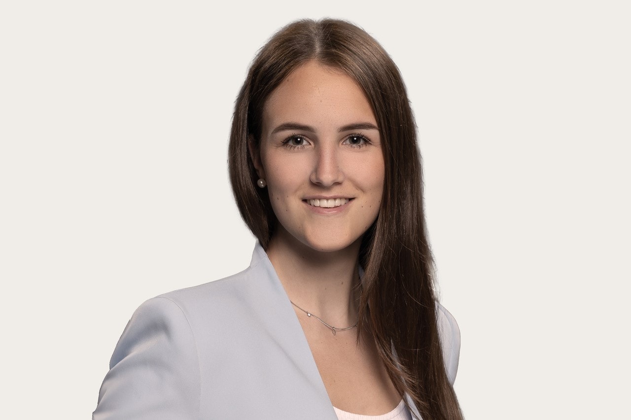 Ein Bild zeigt eine Person mit langen braunen Haaren, die einen hellen Blazer und ein weißes Oberteil trägt.