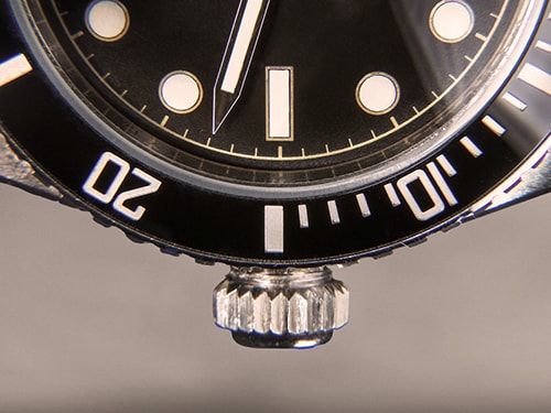 Nahaufnahme einer Armbanduhr mit Fokus auf Lünette und Krone; Markierungen für 10 und 20 Minuten sichtbar.