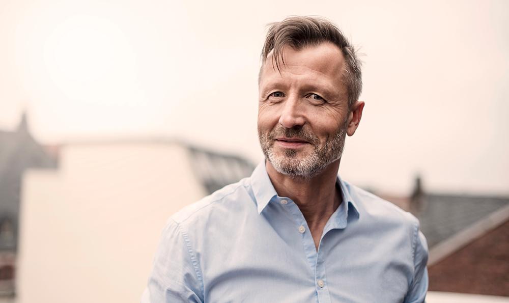 Ein lächender Mann in den Fünfzigern mit leicht ergrautem Haar und Bart lächelt sympatisch in die Kamera