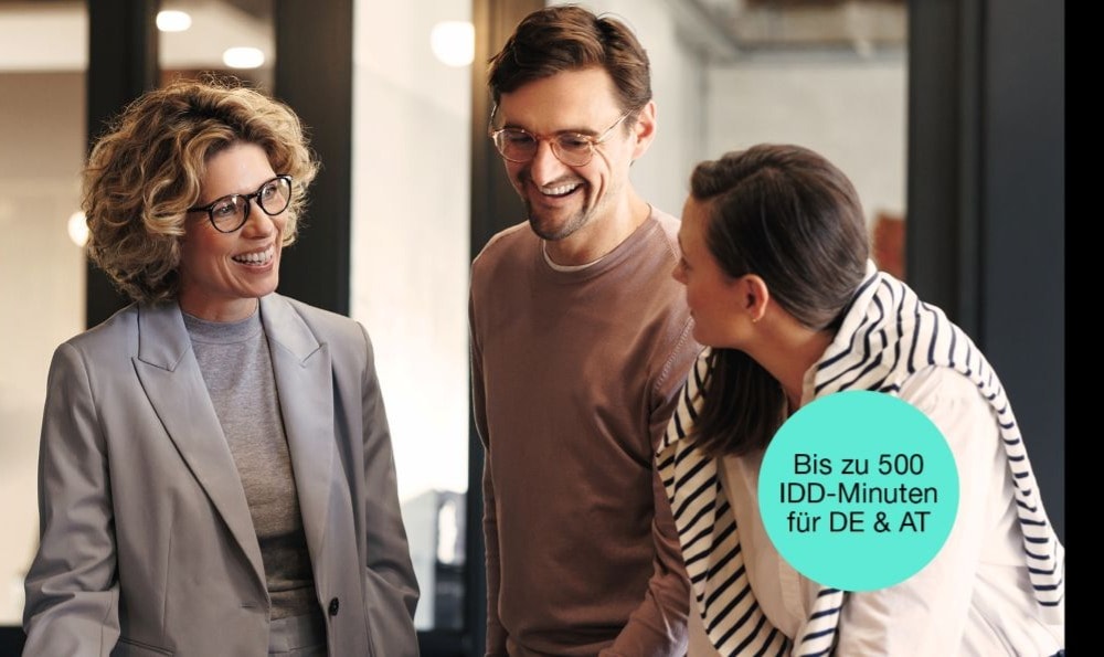 Drei Personen stehen zusammen in einer lockeren Umgebung. Die Person links trägt einen grauen Blazer, die Person in der Mitte ein braunes Langarmshirt und die Person rechts einen gestreiften Schal.