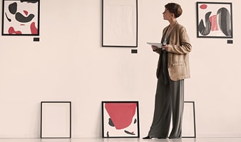 Eine Frau mit Blazer steht vor einer Wand mit Kunstwerken