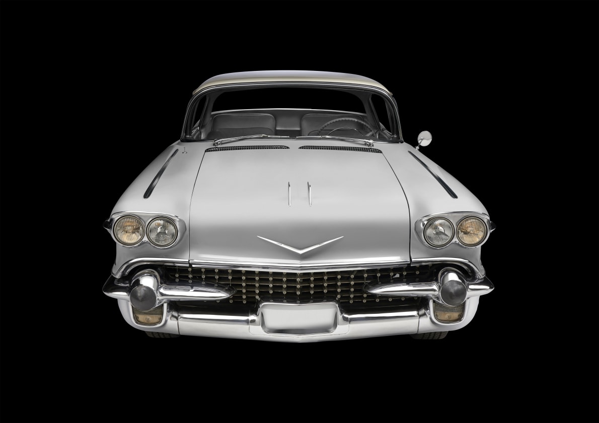Frontansicht eines silbernen Oldtimers mit markantem Kühlergrill, runden Scheinwerfern, Chromdetails und V-förmigem Emblem auf der Motorhaube.