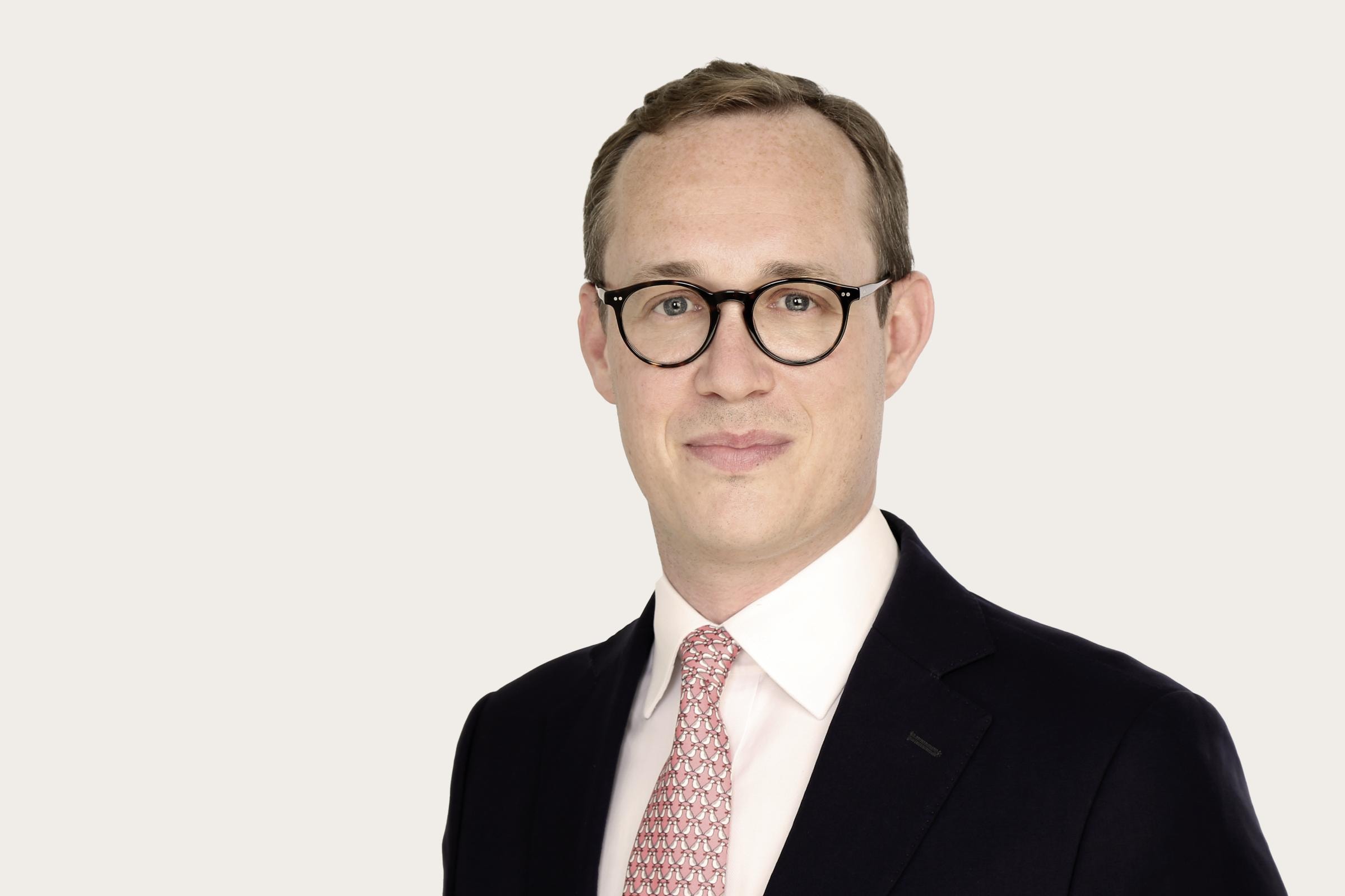 Maximilian Heidbrink, Interim Head of Claims Germany, steht in Anzug mit Krawatte, Hemd und Brille vor einer weißen Wand.