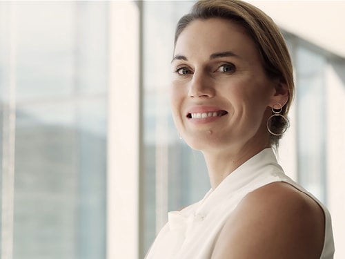 Porträt einer professionell gekleideten Frau in hellem, modernem Büroambiente, die freundlich lächelnd in die Kamera blickt.