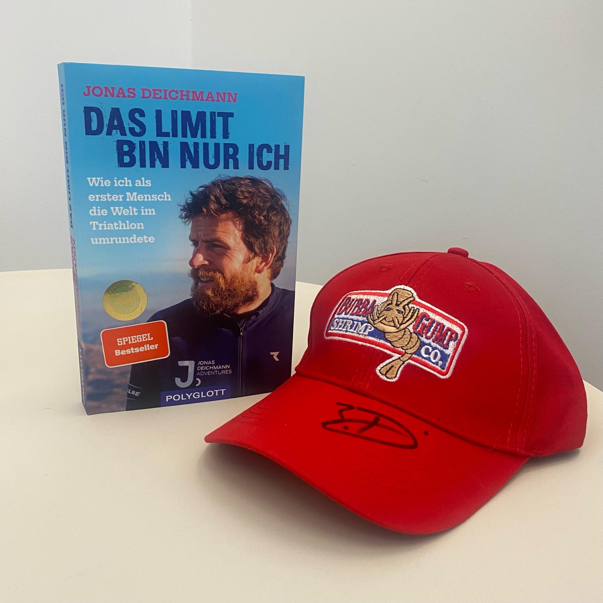 Ein Buch geschrieben von Jonas Deichmann und eine rote Kappe werden auf einem Tisch präsentiert.