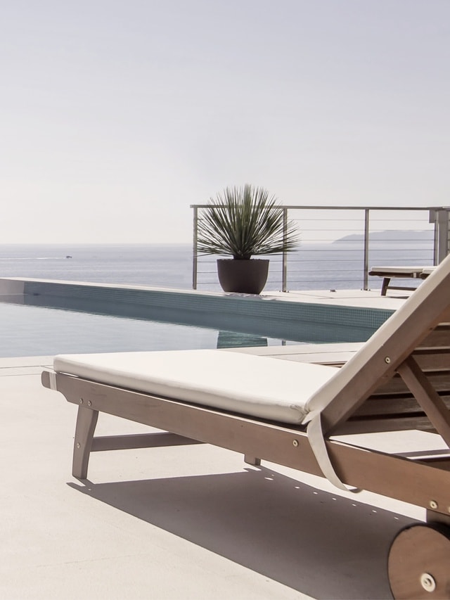 Ein Holzliegestuhl am Pool mit herlichem Ausblick auf das Meer.