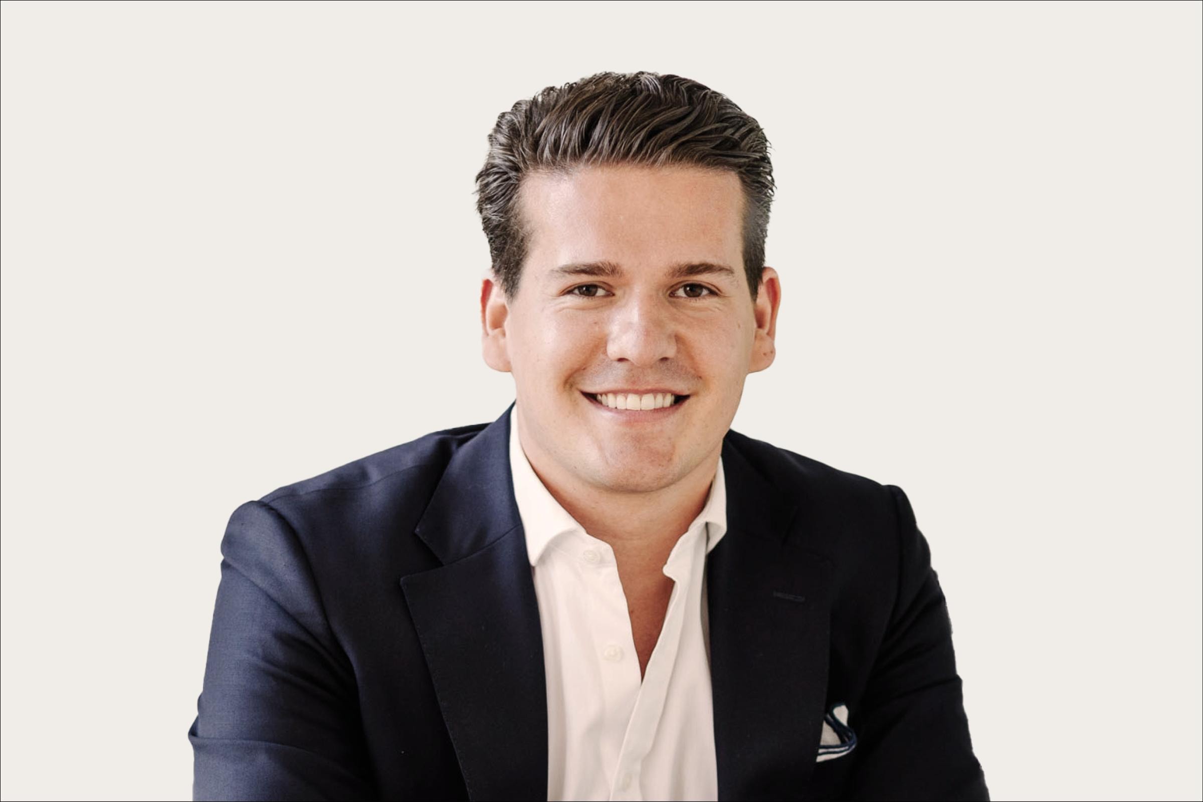 Leon Glaser, ein Man in einem schwarzen Anzug und weißem Hemd, steht vor einem weißen Hintergrund.