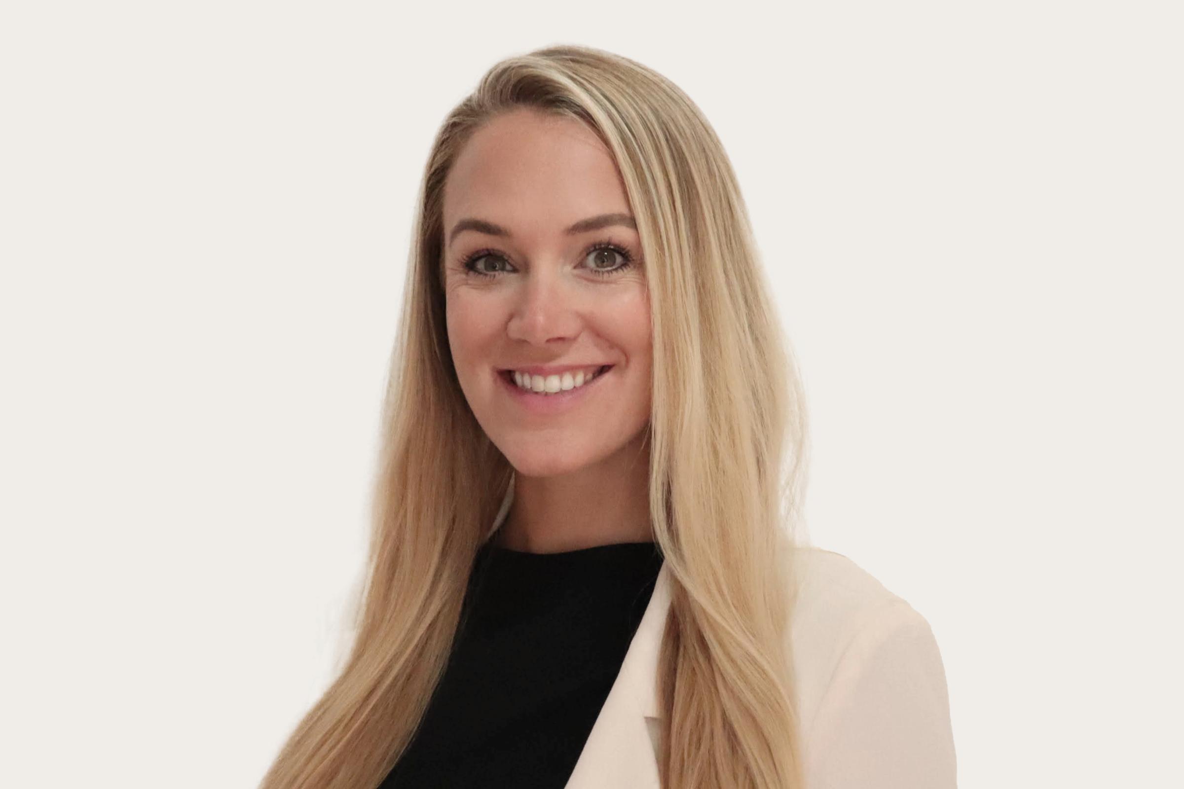 Marie Moeller, eine Frau mit langen blonden Haaren, trägt einen weißen Blazer über einem schwarzen Oberteil.