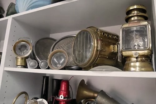 Ein Regal mit verschiedenen alten Schiffsleuchten und Laternen aus Messing. Die Leuchten haben unterschiedliche Größen und Formen und sind auf zwei Regalböden verteilt.