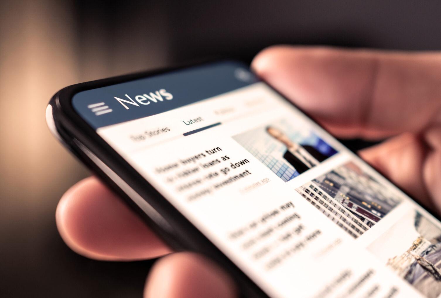 Hand hält ein Mobiles Telefon auf dem eine News-Seite geöffnet ist.
