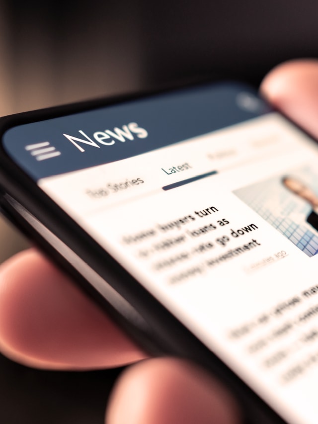 Hand hält ein Mobiles Telefon auf dem eine News-Seite geöffnet ist.