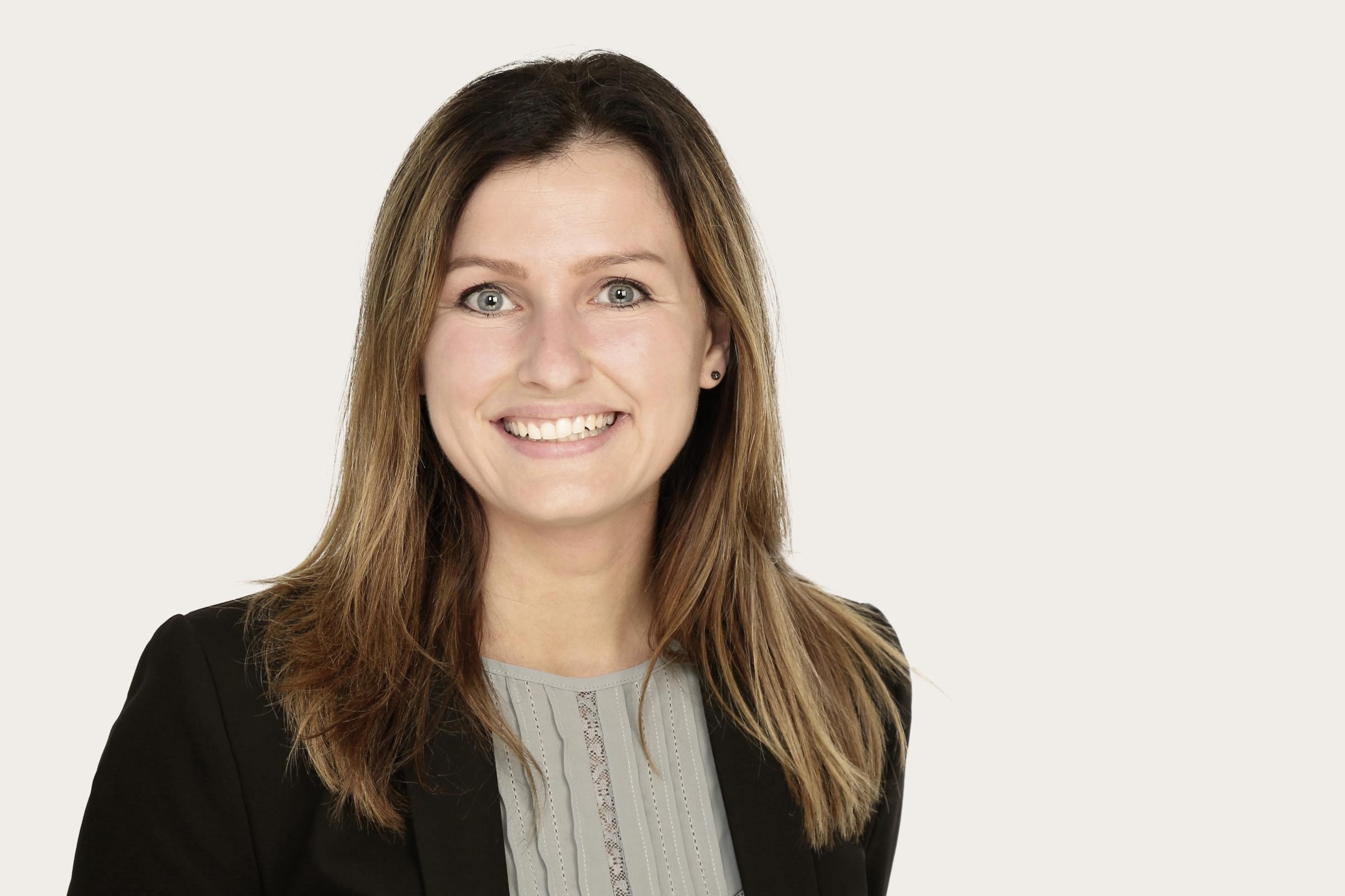 Eine Person mit langen Haaren trägt einen schwarzen Blazer über einem hellen Oberteil. Das Gesicht ist unkenntlich gemacht.